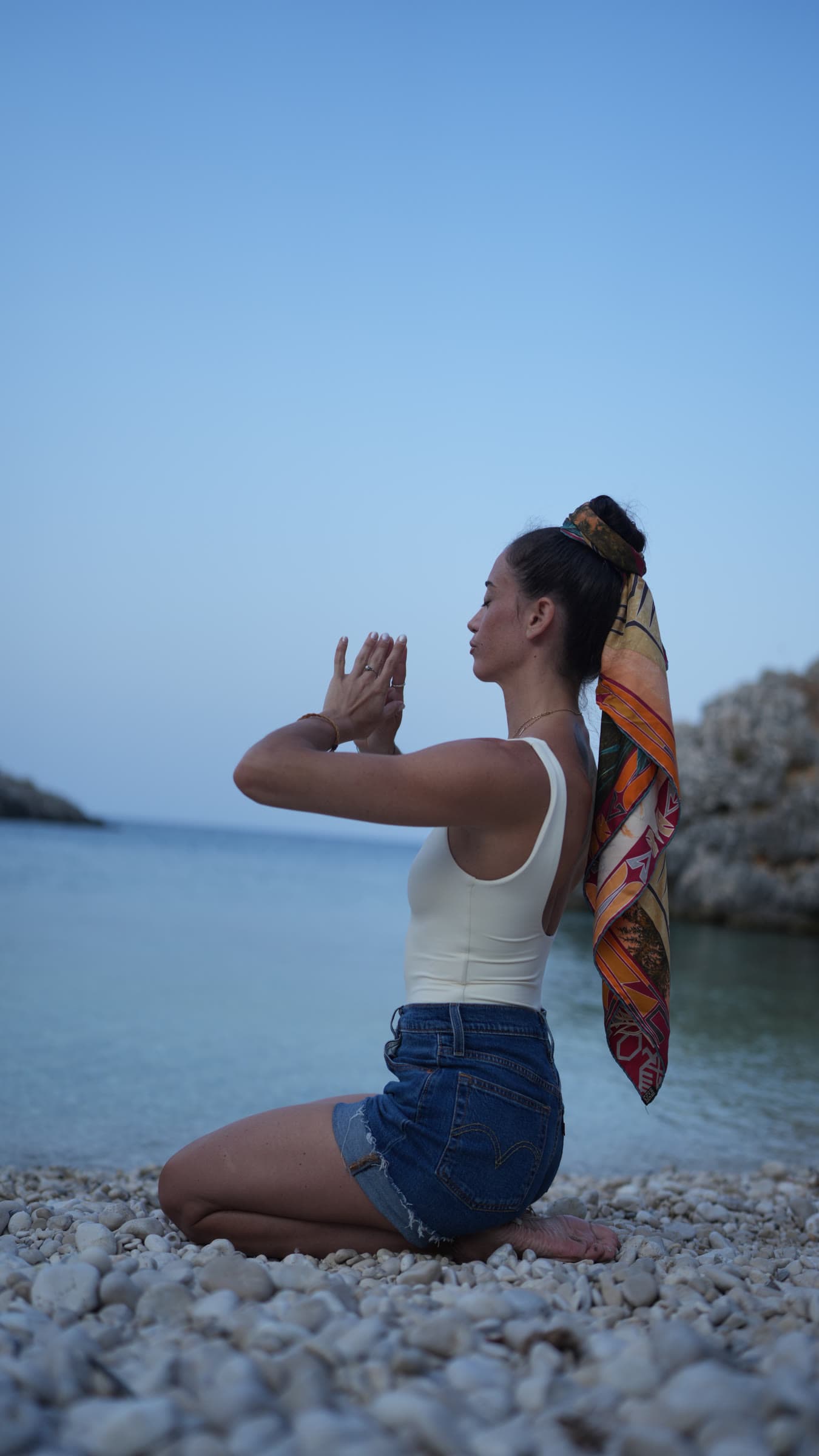 Francesca kneeling on the beach, hands joined in front of her face
