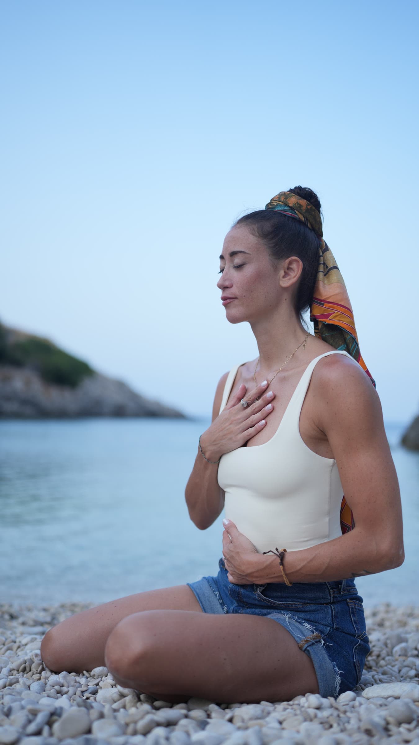Francesca seduta in riva al mare, una mano sul cuore e gli occhi chiusi